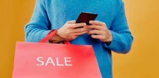 Mężczyzna trzyma w ręku smartfon i torbę z napisem sale