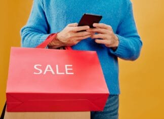 Jak bezpiecznie sprzedać używany telefon przez internet – praktyczne wskazówki dla początkujących Mężczyzna trzyma w ręku smartfon i torbę z napisem sale