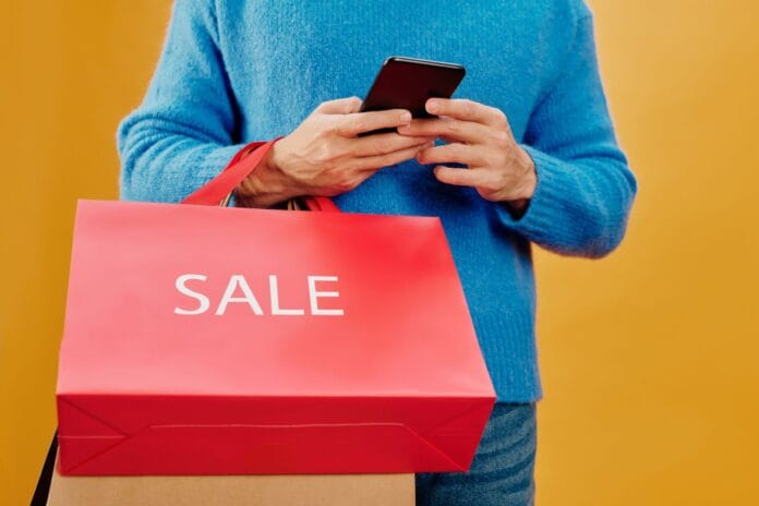 Mężczyzna trzyma w ręku smartfon i torbę z napisem sale